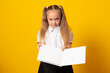 Education and school concept. Smiling little student girl with book. Copy space. Little kid looking at mockup poster and standing on yellow background.