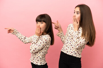 Wall Mural - Little sisters girls isolated on pink background pointing finger to the side with a surprised face