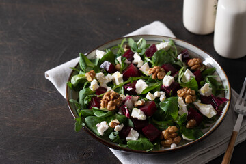 Wall Mural - Beet or beetroot salad with fresh arugula, soft cheese and walnuts on plate, dressing and spices on dark wooden background, copy space, top view