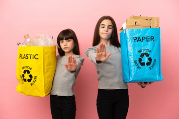 Canvas Print - Little sisters recycling paper and plastic isolated on pink background making stop gesture denying a situation that thinks wrong