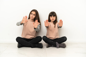 Wall Mural - Little sisters sitting on the floor isolated on white background making stop gesture for disappointed with an opinion