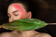 © Lucky33 - Fashionable model with bright makeup posing at the camera holding a green tropical leaf. Woman on black background. High quality photo