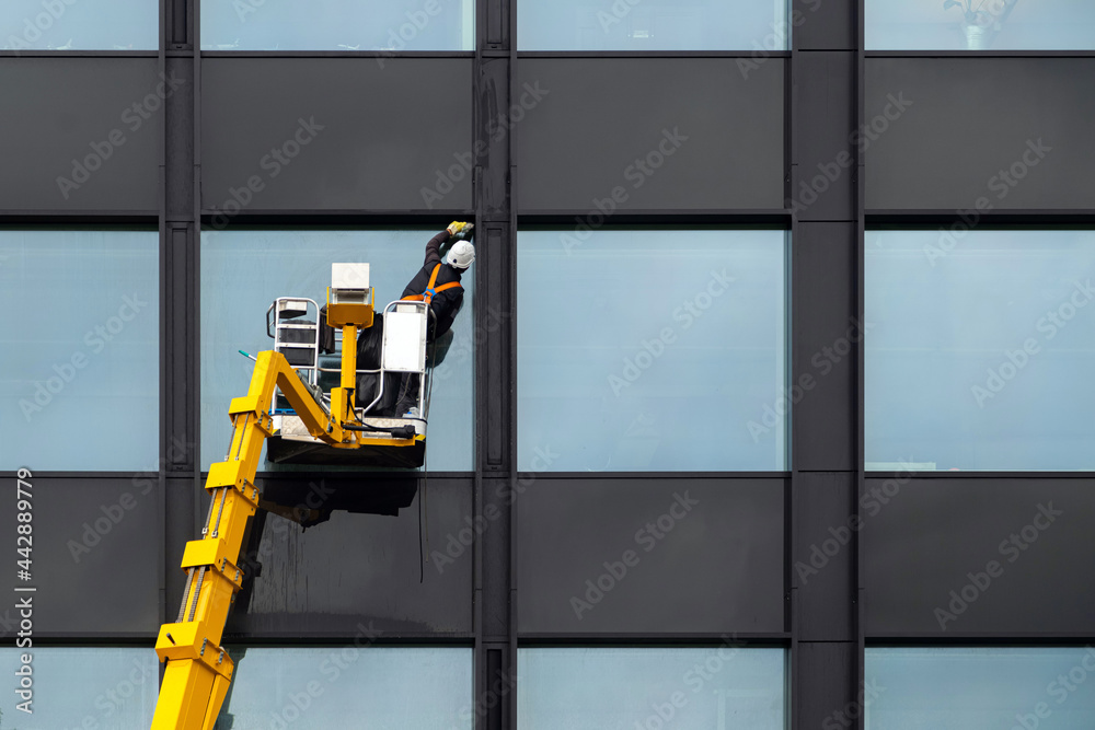 Male window cleaner cleaning glass windows on modern building high in ...