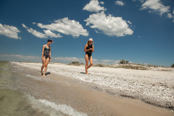 two women in swimsuits looking for a seashell on the seashore in the summer