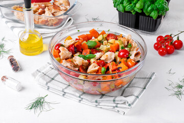 Salad with baked vegetables, croutons, olives, capers, cherry tomatoes, basil and olive oil served in the glass bowl. Mediterranean meal