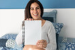 © ADDICTIVE STOCK - Cheerful pregnant woman showing notebook at camera