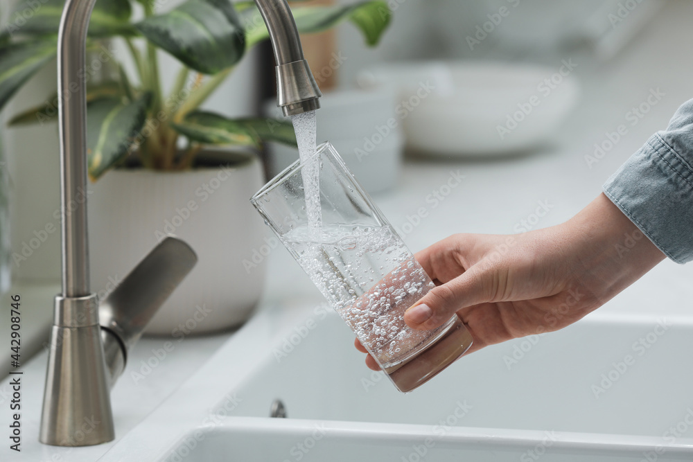Woman filling glass with water from tap in kitchen, closeup - obrazy, fototapety, plakaty 