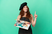 Teenager Redhead Artist Holding A Palette Isolated On Green Background Pointing Up A Great Idea