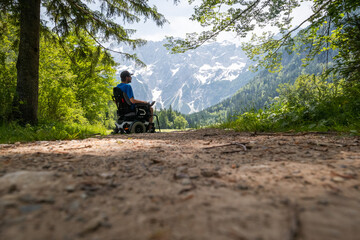 Wall Mural - Man on a wheelchair relaxing in nature and looking at mountains on a sunny summer day.