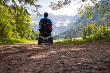 Wall Mural - Man on a wheelchair relaxing in nature and looking at mountains on a sunny summer day.