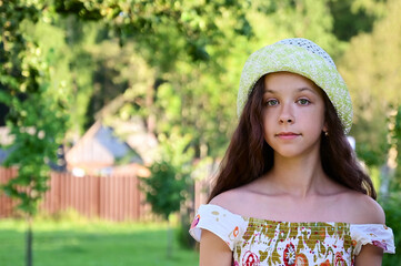 Portrait of a pretty girl with long wavy hair in a hat on the background of a rural landscape. Summer outdoor recreation