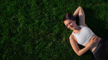 a beautiful, cheerful, cheerful woman in a white t-shirt is lying on the green lawn in the park and 