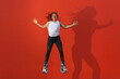 © Julian - Latin, redhead woman in sportswear jumping with open arms wearing Kangoo Jumps boots on orange background. Active movement, action, fitness and wellness concept
