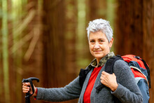 Elderly Caucasian Woman With Backpack Hiking And Looking At Camera Happily. Old Lady Exercising In A Forest.