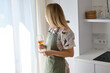 © Iuliia Pilipeichenko - A woman in a kitchen apron and with a glass of white wine in a modern kitchen. Wine tasting. Cooking at home in uniform, protection apparel. Green fabric apron, casual wear