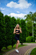 © Hennadii - Young beautiful sporty blonde woman in a black T-shirt and in black tight sports shorts in good shape posing in front of green trees