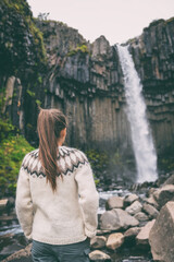 Wall Mural - Iceland. Woman enjoying majestic Svartifoss waterfall. Female is visiting famous tourist attraction of Iceland. Spectacular natural landmark on vacation in Skaftafell. Icelandic nature landscape