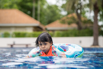 Wall Mural - Little Adorable girl with Inflatable Pool Float at outdoor swimming pool in summer.