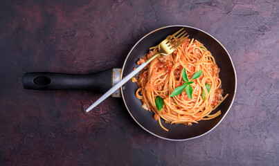 Wall Mural - Appetizing classic Italian spaghetti pasta with tomato and basil sauce and fork arranged on a black pan. On a dark wooden table - top view