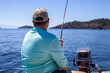 A man holds a fishing rod, trolling for salmon along the coast of British-Columbia, in a small zodiac dinghy wearing a sun shirt and hat