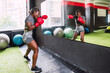 African female athlete practicing boxing in front of a gym mirror. Woman in sportswear in a gym doing routine with boxing gloves