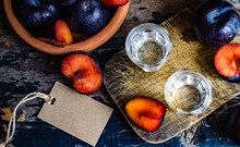 Overhead View Of Two Glass Of Plum Vodka On A Chopping Board With Fresh Plums