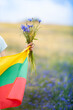 Female hand holding bouquet of blue cornflowers and flag of Lithuania in a rye field. Vertical image. Lithuanian Flag Day. Independence restoration Day. King mindaugas day. Selective focus.