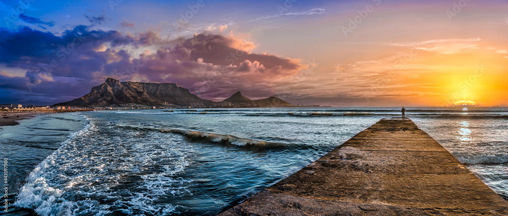 Picturesque and colourful sunset scene of Table Mountain and The Atlantic Ocean. A jetty reaches out to the cool blue sea to inspire a sense of adventure. A stunning tourist destination - Cape Town - obrazy, fototapety, plakaty 