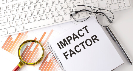 IMPACT FACTOR text written on a notebook with keyboard, chart,and glasses