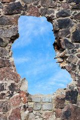 Canvas Print - an old wall of natural stone with a hole from which you can see the blue sky with clouds