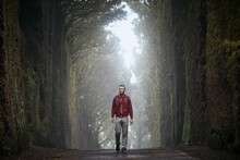 Man Is Walking Along Road Between Rocks In The Middle Of Mysterious Foggy Forest. Tenerife, Canary Islands, Spain.
