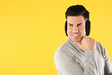 Wall Mural - Man wearing stylish earmuffs on yellow background. Space for text