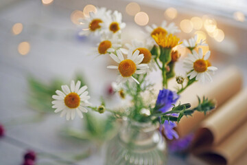 Wall Mural - Small bouquet of wild flowers daisies in a glass vase on a wooden table. Summer background concept