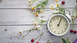 Summer time background. White alarm clock arrows noon on a wooden table around wildflowers fresh berries. Summer background concept, copy space