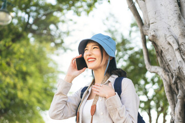 Wall Mural - Young adult asian woman traveller wear blue hat and backpack using mobile phone internet for calling on travel.