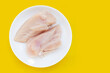 Uncooked raw chicken  breast fillets in white plate on yellow background.