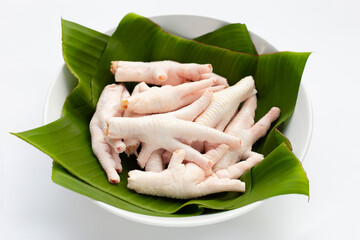 Raw chicken feet in white bowl wih banana leaves on white background