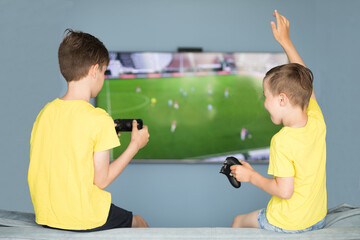 Boys play in football video game. One of them celebrates a goal