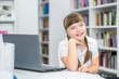 Smiling young girl with syndrome down sits with a laptop at library. Education for disabled children concept