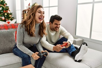 Young hispanic couple smiling happy sitting on the sofa playing video game at home.