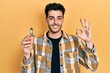 Young hispanic man holding electronic cigarette doing ok sign with fingers, smiling friendly gesturing excellent symbol