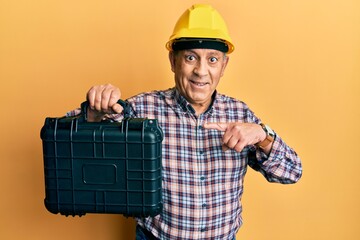 Poster - Handsome senior man with grey hair wearing safety helmet holding toolbox smiling happy pointing with hand and finger