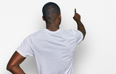 Young african american man wearing casual white t shirt posing backwards pointing ahead with finger hand