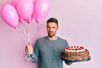 Poster - Handsome man with beard celebrating birthday with cake holding balloons clueless and confused expression. doubt concept.