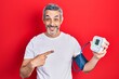 Handsome middle age man with grey hair using blood pressure monitor smiling happy pointing with hand and finger