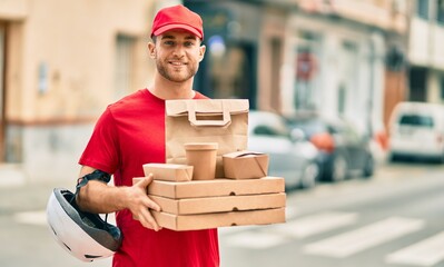 Canvas Print - Young caucasian deliveryman smiling happy holding delivery food at the city.