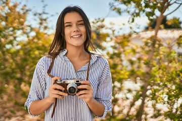 Wall Mural - Young hispanic tourist girl smiling happy using camera at the park