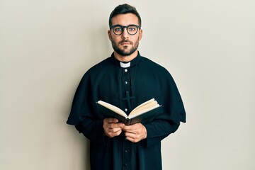 Canvas Print - Young hispanic priest man holding bible relaxed with serious expression on face. simple and natural looking at the camera.