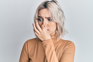 Poster - Young blonde girl wearing casual clothes smelling something stinky and disgusting, intolerable smell, holding breath with fingers on nose. bad smell