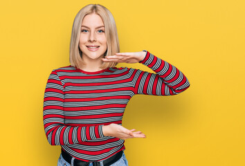 Young blonde woman wearing casual clothes gesturing with hands showing big and large size sign, measure symbol. smiling looking at the camera. measuring concept.